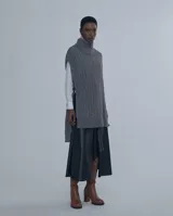 Chaleco largo de punto trenzado color gris con cuello alto y cierre frontal con cremallera metálica.