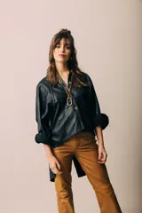 Camisa de cuero negro con corte asimétrico, más larga en la parte posterior, con botones frontales y tajo central en la espalda.