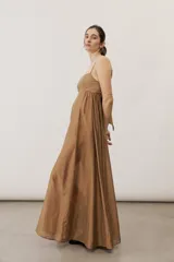 Vestido largo color beige con escote recto, tirantes finos y falda amplia con diseño drapeado.