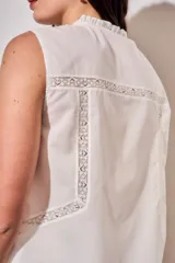 Blusa sin mangas de algodón color blanco off white, con cuello redondo y cierre frontal mediante cordones para atar. Presenta delicados detalles de bordados tonales e inserciones de encaje vertical en el frente.