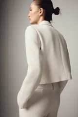 Blazer corto de cuello solapa y manga larga con hombreras. Presenta un diseño cruzado con cierre frontal de dos botones dorados.