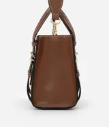Cartera satchel mediana de color marrón, confeccionada en poliuretano con diseño estructurado, costuras en contraste y herrajes metálicos dorados. Cuenta con doble asa de mano, correas decorativas verticales con hebillas en la parte frontal y una correa larga ajustable y desmontable para llevar al hombro o cruzada.