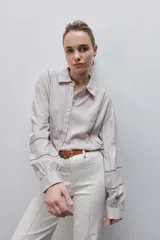 Camisa de viscosa color gris claro, de calce amplio y caída fluida, con cuello clásico, cierre frontal con botones y detalles calados en mangas y delantero.