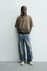 Camiseta de corte relajado (relaxed fit) con cuello redondo y manga corta. Presenta un estampado frontal con relieve en la zona del pecho con el texto "Endless Echo", y un efecto de teñido degradado que va del marrón claro al marrón oscuro/negro en la parte inferior.