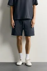 Bermuda estilo jogger de ajuste relajado, confeccionada en tejido interlock de algodón. Cuenta con cintura elástica ajustable con cordón, bolsillos frontales de vivo y diseño liso.