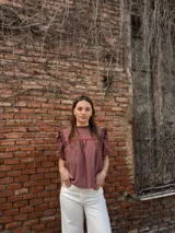 Blusa color chocolate con mangas cortas abullonadas, cuello redondo con volados y detalles de costura en zigzag de color rojo en el pecho y volados oscuros en los hombros.