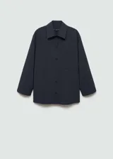 Camisa de corte recto con diseño de raya diplomática, cuello camisero, cierre frontal de botones y dos bolsillos de parche delanteros. Presenta mangas largas con puños rectos.