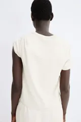 Remera color crema de punto de algodón tupido con cuello redondo ribeteado acanalado y mangas cortas.