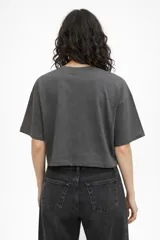 Remera de algodón color gris topo, de corte holgado y diseño cropped. Presenta cuello redondo y una estampa frontal con forma de corazón, mariposa y texto decorativo.