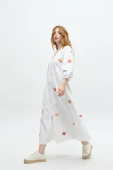 Vestido largo blanco de algodón con bordados de motivos marinos en tonos naranja, verde y azul. Tiene escote en V, mangas 3/4 abullonadas y cierre frontal con botones.