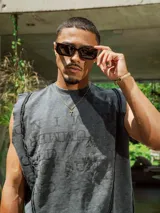 Musculosa sin mangas color gris oscuro con efecto lavado y bordes deshilachados. Presenta un estampado en relieve en el frente con texto en mayúsculas.