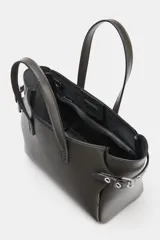 Bolso mini shopper de color gris oscuro, con diseño estructurado, doble asa de mano y correas laterales decorativas con hebillas metálicas. Incluye cierre magnético y compartimento interior con cremallera.