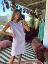 Vestido corto color lila, sin mangas, con detalle de volados plisados verticales en los laterales del frente.