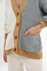 Cárdigan tejido de punto grueso, con diseño color block en gris, blanco y beige. Tiene cuello en V, cierre frontal con botones y un bolsillo de parche.
