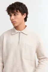 Sweater de punto color beige con cuello polo, cierre frontal parcial y bolsillo en el pecho. Presenta mangas largas con puños acanalados y diseño de corte recto.