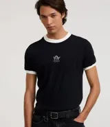 Remera de algodón negra, estilo ringer, con cuello y ribetes de manga en color blanco contrastante. Presenta un pequeño bordado de un ángel en el centro del pecho.