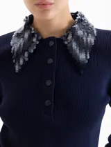 Top de punto acanalado color azul marino, con mangas largas y cuello camisero bordado con lentejuelas al tono. Presenta cierre frontal con broches metálicos.
