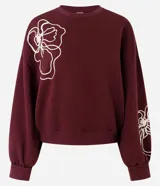 Buzo de algodón color bordó con cuello redondo acanalado, mangas largas con puños ajustados y terminación inferior elástica. Presenta un diseño de bordado floral en cuerda de color crudo en el frente y en una de las mangas.