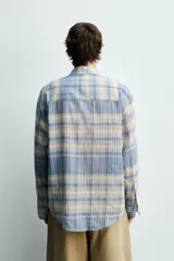 Camisa de corte relajado confeccionada en tejido ligero de algodón, con diseño de cuadros en tonos azules y beige. Presenta cuello solapa, cierre frontal de botones, manga larga con puño abotonado y un bolsillo en el pecho.