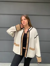 Chaqueta color crema con ribetes en marrón y negro, de lana merino, con cuello redondo, cierre frontal con botones y bolsillos de parche.