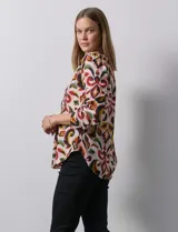 Blusa de gasa estampada con diseño geométrico multicolor, cuello a la base con escote en V y abertura frontal con botones. Presenta detalle de plisado en la parte delantera y mangas largas con sistema de ajuste mediante presilla y botón.