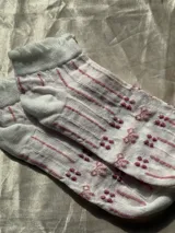 Medias cortas blancas con diseño estampado de rayas verticales rosadas y pequeños moños, con elástico ondulado en el borde superior.