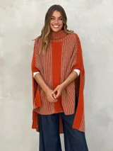 Poncho de punto color naranja y beige con rayas verticales, cuello alto y aberturas laterales.