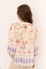 Blusa de manga tres cuartos color beige con estampado floral multicolor, escote en V y detalles de volados frontales junto a la botonadura.