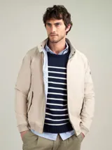 Campera Harrington color beige, con cuello alto abotonado, cierre frontal completo y bolsillos laterales con solapa y botones a presión. Puños y cintura elastizados de rib.