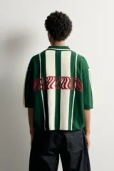 Polo de punto boxy fit color verde oscuro y blanco, de manga corta, con cuello solapa, cierre frontal con botones y detalle de texto bordado a contraste en el pecho.