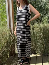 Vestido largo de punto a rayas horizontales negras y blancas, sin mangas, con cuello redondo y volados blancos en cuello y sisas.