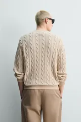 Sweater de punto con diseño de trenzas, color beige, cuello redondo y manga larga con terminaciones en rib.