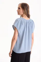 Blusa negra de manga corta, confeccionada en tela crepé, con detalle de fruncido en el escote redondo y pequeña abertura frontal en V.