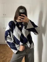 Sweater de tejido de punto con diseño de rombos argyle en color azul marino y gris, de cuello redondo y mangas largas holgadas.