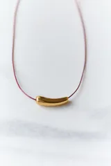 Gargantilla minimalista compuesta por un hilo encerado fino y un dije central de acero quirúrgico en forma de tubo curvo.