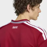 Camiseta de fútbol Adidas del Manchester United, modelo Home 26/27. Diseño en color rojo con cuello polo y puños a rayas en blanco y negro, con detalles de las tres tiras de Adidas en los hombros y el logo de Snapdragon en el frente.