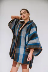 Ruana confeccionada en paño italiano con diseño a cuadros en tonos gris, azul y negro, con terminaciones ribeteadas en cuerina color camel y botón en las mangas.