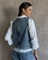 Chaleco de corte recto y largo a la cintura, confeccionado en denim con estampado de rayas verticales en tonos azul y blanco. Presenta cuello redondo y costuras visibles que definen su estructura.