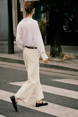 Pantalón de vestir color beige, tiro alto, corte ancho y pierna recta. Presenta un bajo con vuelta y viene acompañado de un cinturón fino de cuero marrón con hebilla metálica.