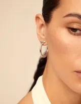 Aros de metal bañados en plata, de diseño abierto con forma de argolla y una pequeña barra perpendicular en la parte superior.