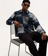 Campera de jacquard de algodón con diseño patchwork de cuadros en tonos azules. Presenta cuello inglés, cierre frontal con botones metálicos, mangas largas y bolsillos delanteros.