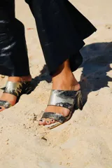 Sandalias de tacón alto con diseño de dos tiras anchas, confeccionadas en tela con estampado abstracto en tonos dorados y negros. Presentan un tacón cuadrado forrado en el mismo tejido.