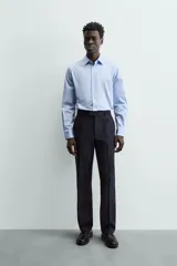 Camisa de manga larga, color blanco, con cuello italiano y corte slim fit. Presenta cierre frontal de botonadura y puños con botón.