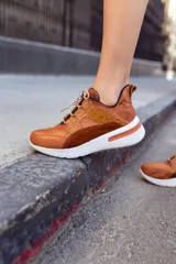 Championes deportivos de cuero en tonos marrón, tostado y marrón oscuro, con detalles de estampado animal print de leopardo en el lateral, suela gruesa blanca y cordones elásticos.