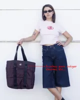 Bolso tipo tote de diseño urbano, confeccionado en material impermeable acolchado de color negro. Cuenta con doble asa de hombro, compartimento principal con cierre, bolsillo frontal con cierre y detalle de logo circular en la parte superior.