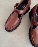 Zapato tipo guillermina marca Lucy in the Sky, confeccionado en cuero vacuno color marrón. Presenta costuras decorativas en el borde superior, cierre con hebilla lateral y suela track negra de goma.