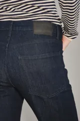 Jean de corte recto y tiro medio, confeccionado en denim azul oscuro de acabado raw. Presenta un diseño clásico de cinco bolsillos con costuras reforzadas y cierre frontal con botón y cremallera.