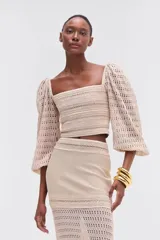 Top cropped de color beige con escote cuadrado y mangas largas abullonadas, confeccionado en tejido calado con forro y cremallera metálica en la espalda.