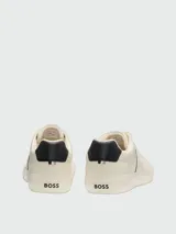 Zapatillas Boss modelo Aiden Tenn Grained, color blanco marfil con detalles en negro en el talón y líneas laterales, con la inscripción de la marca en el lateral.