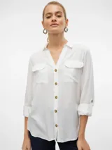 Camisa de color blanco, de mangas largas con opción de vuelta mediante botón, con bolsillo frontal en el pecho, cuello camisero y dobladillo redondeado.